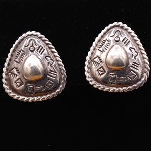 May include: A pair of silver earrings with a triangular shape and a textured design. The earrings feature a raised, rounded center piece and intricate geometric patterns.