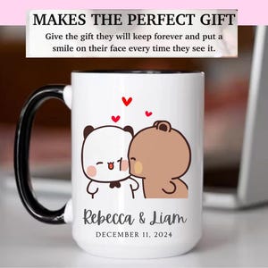 May include: White ceramic mug with a black handle and rim. The mug features a cartoon panda and bear kissing, with red heart accents. The names "Rebecca & Liam" and the date "DECEMBER 11, 2024" are printed on the mug.