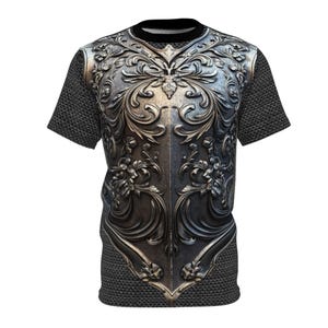 Pode incluir: Camiseta de manga curta com um design detalhado e ornamentado de armadura prateada na frente. O design da armadura apresenta intrincados padrões florais e de rolagem. As mangas e a parte superior das costas têm um padrão de malha de corrente. Gola redonda preta.