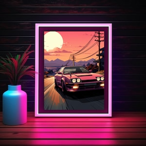May include: Framed artwork of a pink sports car on a road at sunset. The artwork has a pink border and is displayed on a wooden surface. A vase with a plant is on the left.