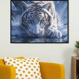 May include: A white tiger with blue eyes stares intensely at the viewer. The tiger is lying in a snowy forest setting with a reflection of the tiger in the water below.