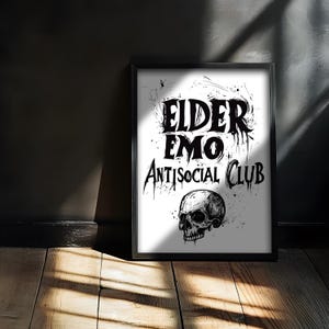 Può includere: Stampa grafica in bianco e nero con il testo "Elder Emo Antisocial Club" e un'illustrazione di teschio.