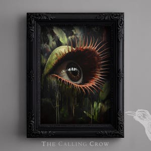 May include: A framed artwork featuring a close-up of a plant eye with a brown iris and red, spiky edges. The eye is surrounded by green leaves and dark, dripping elements. The black frame has ornate detailing, and the text "THE CALLING CROW" is at the bottom.