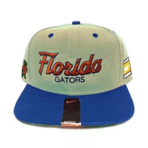 May include: A light green and blue baseball cap with the words "Florida Gators" embroidered in orange and white. The cap has a Nike logo on the front.
