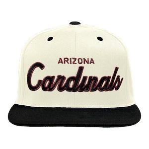 May include: White baseball cap with a black brim. The front of the cap has the words "Arizona Cardinals" embroidered in black and maroon.