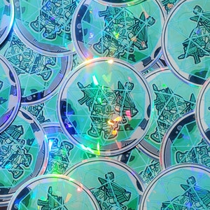 May include: A collection of holographic stickers featuring a green and black robot design. The stickers are circular and have a shiny, iridescent finish.