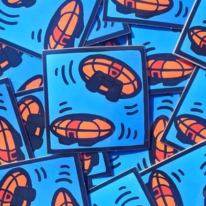 Puede incluir: Un conjunto de pegatinas coloridas con un diseño de platillo volante. Las pegatinas están sobre un fondo azul con contornos blancos y detalles negros. Las pegatinas son perfectas para agregar un toque de fantasía a las computadoras portátiles, las botellas de agua o los cuadernos.