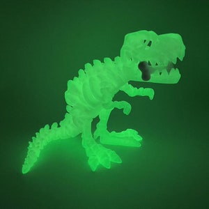 May include: A green glow-in-the-dark dinosaur skeleton toy. The dinosaur is posed in a standing position with its mouth open and a bone in its mouth.
