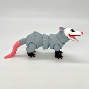 May include: A gray and pink articulated possum toy with a segmented tail and black eyes. The possum is posed standing on all fours with its mouth open.