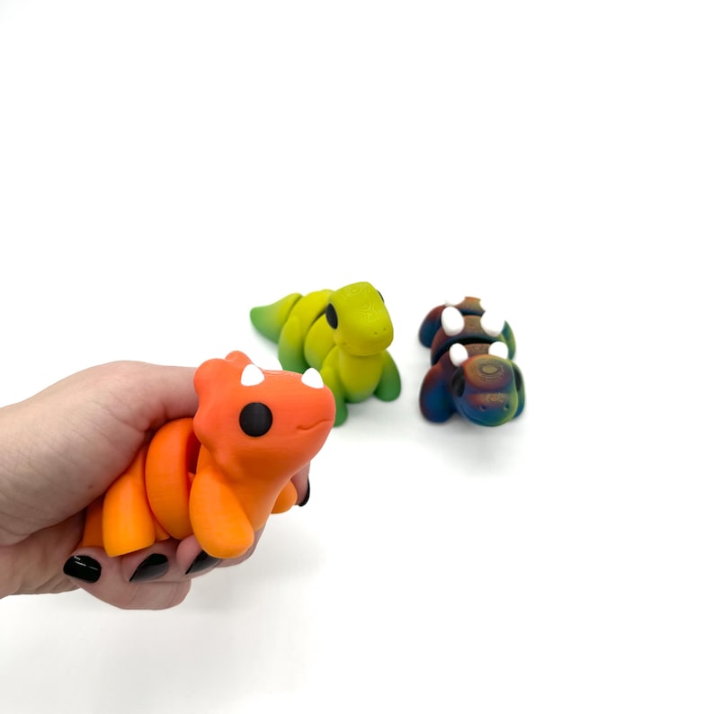 May include: Three small, colourful, hand-painted dinosaur figurines. One is orange and red, one is green and yellow, and one is blue and purple.