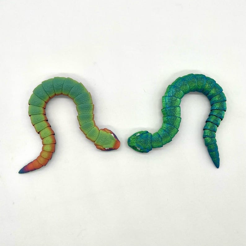 May include: Two green and iridescent segmented plastic toy snakes with a slight bend in their bodies. The snakes are facing each other with their heads touching.