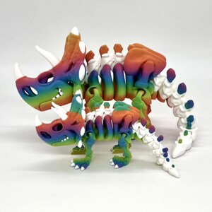 May include: A rainbow colored 3D printed skeleton of a triceratops and a smaller dinosaur. The skeletons are articulated and poseable.