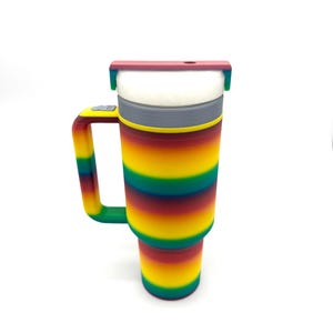 May include: A colorful insulated tumbler with a handle. The tumbler features a rainbow striped design in shades of red, orange, yellow, green, and blue. It has a white interior and a red lid. The handle is green.