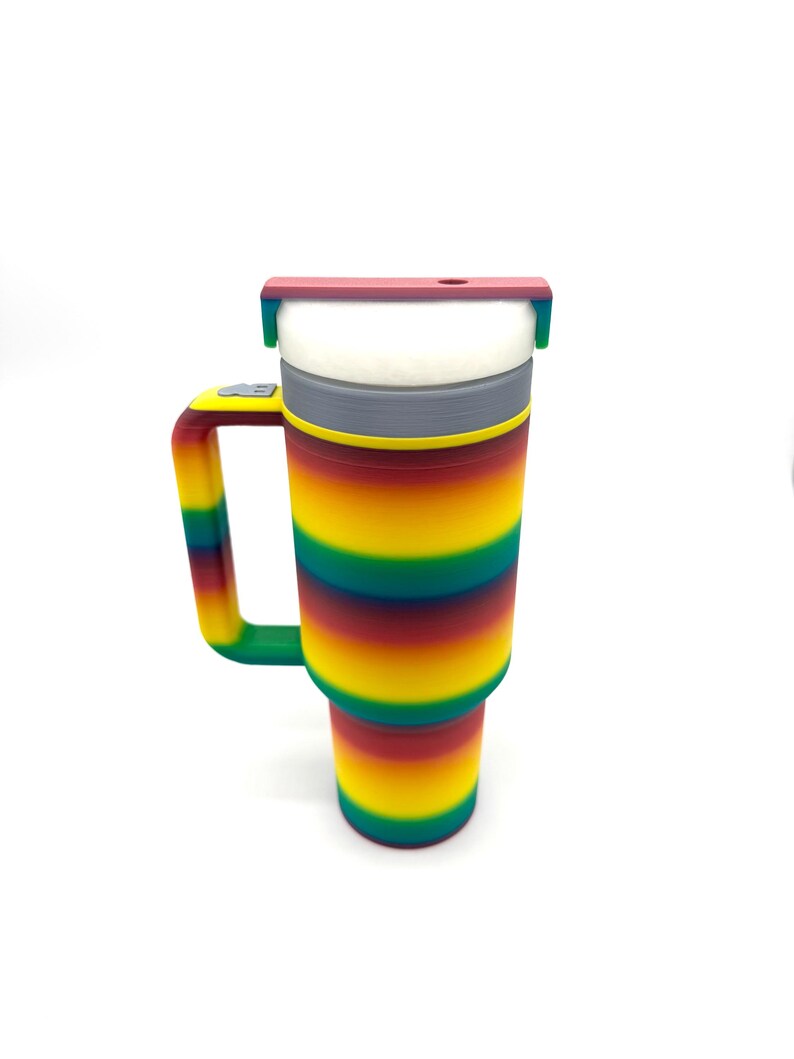May include: A colorful insulated tumbler with a handle. The tumbler features a rainbow striped design in shades of red, orange, yellow, green, and blue. It has a white interior and a red lid. The handle is green.