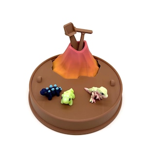 May include: A brown, circular toy playset featuring a volcano with a pink and orange gradient, and a set of wooden tools. Three small, colorful dinosaur figurines are placed around the volcano, including a blue one with light blue spikes.