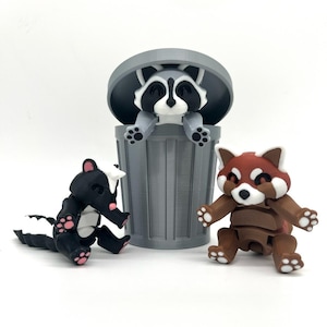 May include: Three small, articulated animal figurines: a raccoon in a gray trash can, a red panda, and a skunk. The raccoon is sitting in the trash can with its head poking out of the top. The red panda is sitting on the ground with its arms outstretched. The skunk is sitting on the ground with its tail curled up.