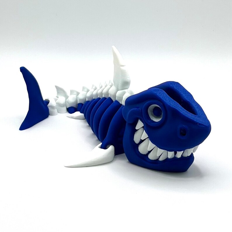 May include: A blue and white 3D printed shark skeleton toy. The shark has a toothy grin and a white spine.