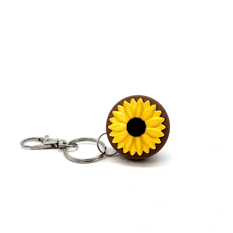 May include: A brown wooden keychain with a yellow sunflower design. The keychain has a silver split ring and a silver lobster clasp.