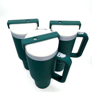 May include: Three dark green insulated mugs with white interiors and gray rims are displayed against a white background. Each mug has a handle and a dark green lid with a small opening. The mugs are designed to keep beverages hot or cold.