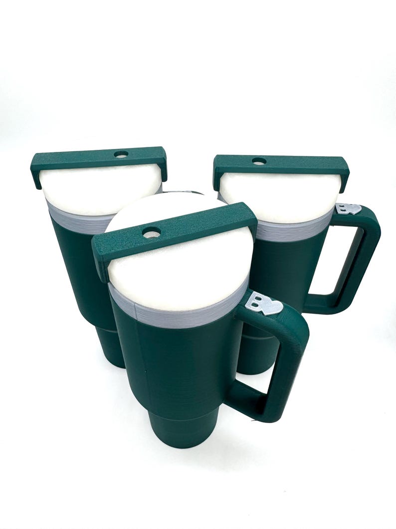 May include: Three dark green insulated mugs with white interiors and gray rims are displayed against a white background. Each mug has a handle and a dark green lid with a small opening. The mugs are designed to keep beverages hot or cold.