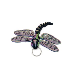 May include: A black and iridescent dragonfly keyring with a silver ring. The dragonfly has a detailed, intricate design on its wings.