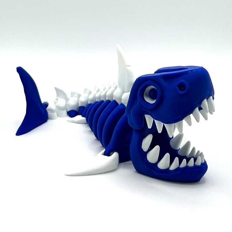 May include: A blue and white plastic toy shark with a skeleton design. The shark has a large open mouth with white teeth and a white dorsal fin.