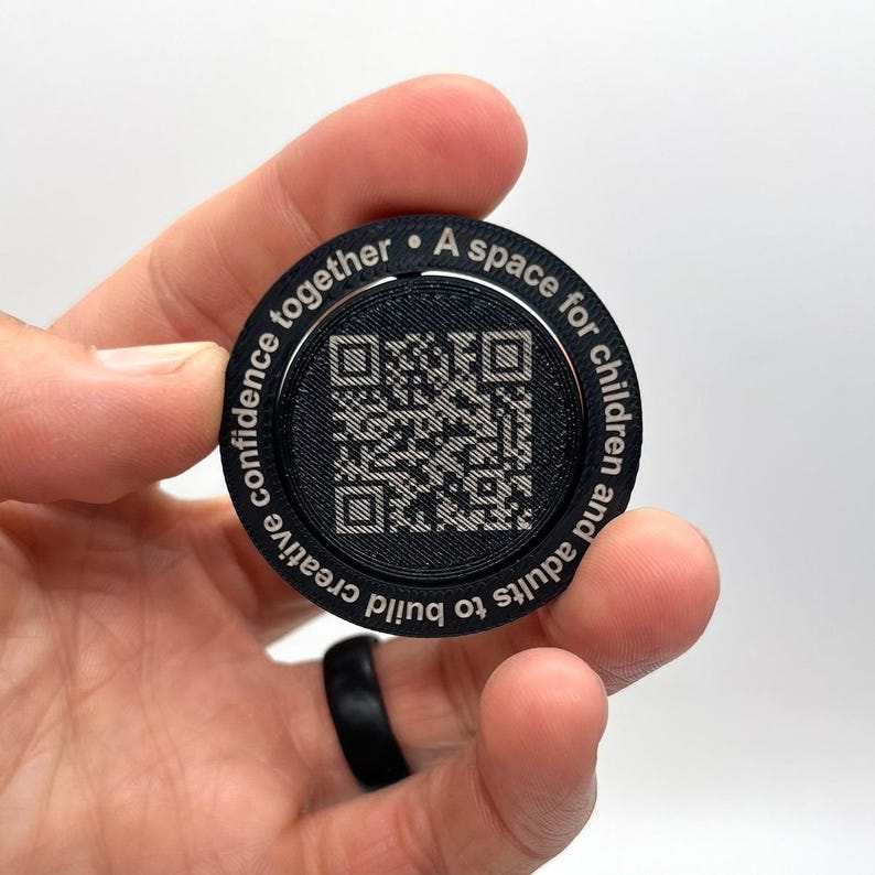 May include: Black round disc with a QR code in the center and the text "A space for children and adults to build creative confidence together." around the edge.