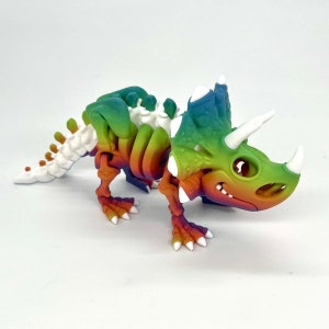 May include: A rainbow-colored plastic dinosaur skeleton toy with white accents. The dinosaur is a triceratops with three horns and a frill.
