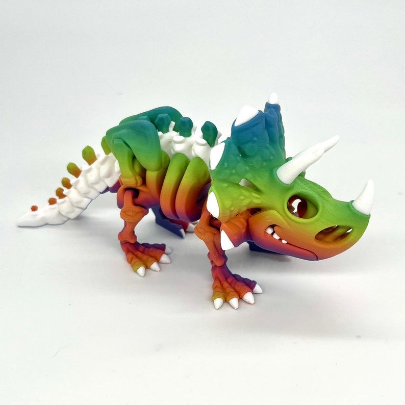 May include: A rainbow-colored plastic dinosaur skeleton toy with white accents. The dinosaur is a triceratops with three horns and a frill.