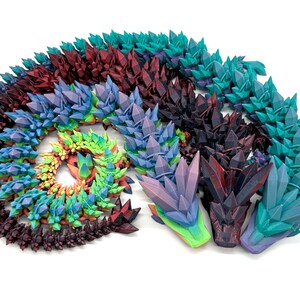 May include: A colorful set of 3D printed dragon heads with a crystal-like texture. The heads are arranged in a spiral pattern and are made in a variety of colors, including purple, blue, green, and red.