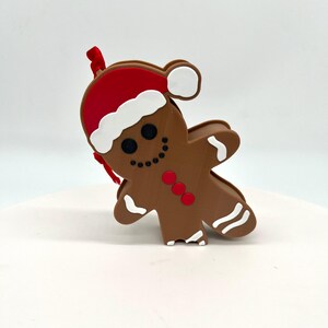 May include: A brown gingerbread man ornament with white icing and red buttons. The gingerbread man is wearing a red and white Santa hat.