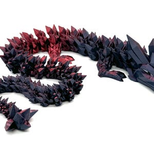 May include: A black and red crystal dragon figurine with a long, curled tail. The dragon is made of a shiny, textured material and has a detailed design.