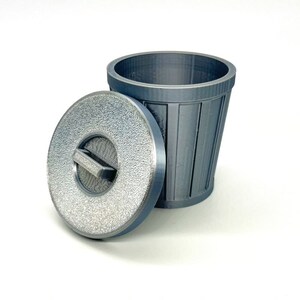 May include: A silver metal trash can with a lid. The lid has a textured surface and a small handle.