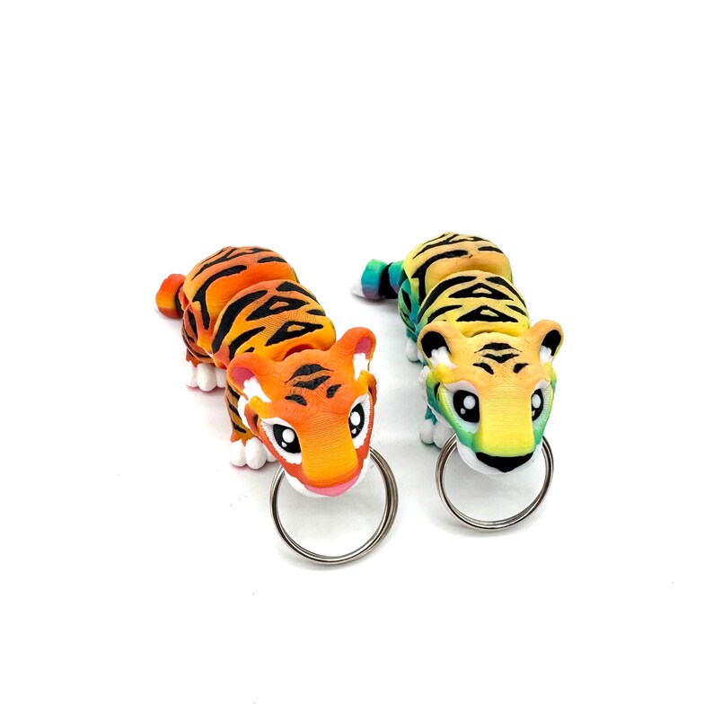 May include: Two tiger-shaped keyrings, one orange and black, the other yellow and green, with a rainbow gradient. Both have a silver key ring.