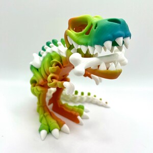 May include: A colorful, articulated dinosaur skeleton toy with a gradient of green, orange, and yellow. The dinosaur is holding a white bone in its mouth.