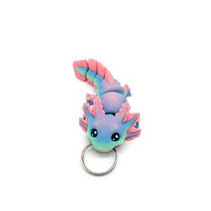 May include: A pink and blue axolotl keychain with a silver key ring. The axolotl is a small, aquatic salamander with feathery gills.