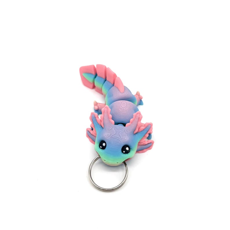 May include: A pink and blue axolotl keychain with a silver key ring. The axolotl is a small, aquatic salamander with feathery gills.