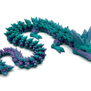 May include: A teal and purple crystal dragon figurine with a spiky, textured body. The dragon is posed with its head raised and its tail curled.