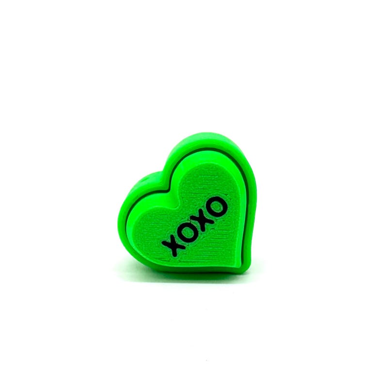 May include: A bright green heart-shaped candy with the word "XOXO" printed on it.