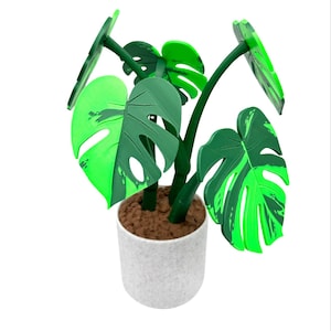 K&ouml;nnte beinhalten: Eine kleine k&uuml;nstliche Monstera-Pflanze in einem wei&szlig;en, gesprenkelten Topf. Die Pflanze hat gro&szlig;e, gr&uuml;ne Bl&auml;tter mit einem geteilten Blattdesign. Die Bl&auml;tter haben verschiedene Gr&uuml;nt&ouml;ne, und der Topf ist mit braunem, strukturiertem Material gef&uuml;llt.