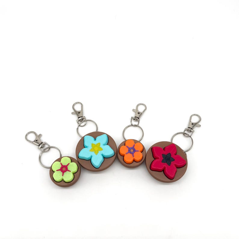 May include: Four keychains with brown circular bases and colorful flower designs. The flowers are blue, red, orange, and green.