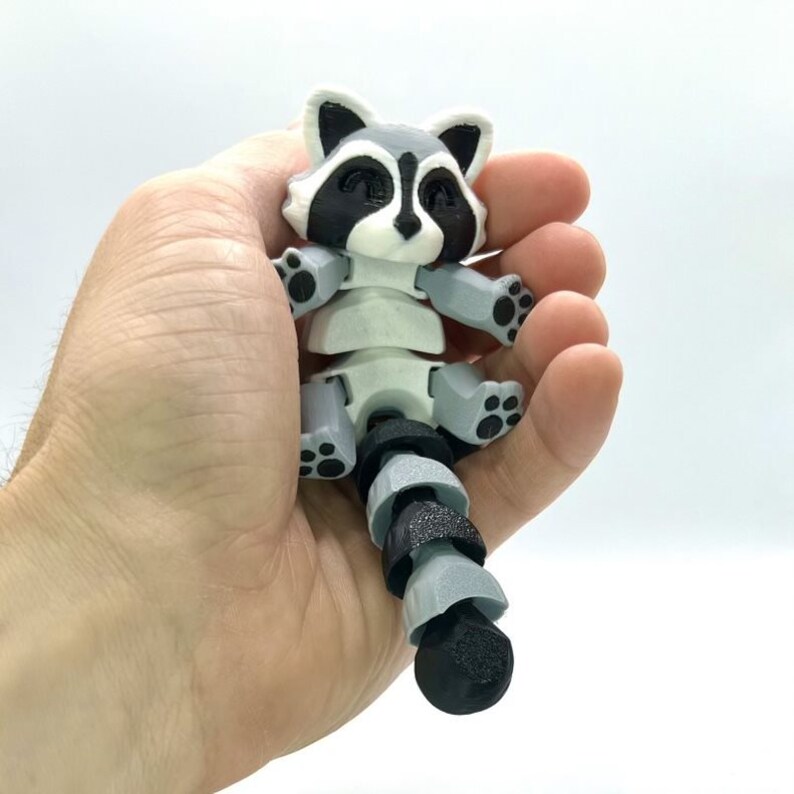May include: A white and gray articulated raccoon figurine with a black and gray segmented tail. The figurine has black eyes and a black nose.