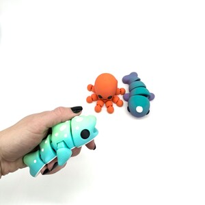 May include: Three colourful, articulated, bendable, and posable plastic toys shaped like a fish, an octopus, and a fish. The toys are made of a soft, flexible material and have a fun, cartoonish design.