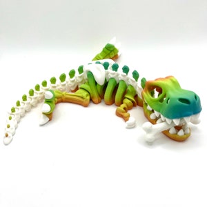 May include: A colorful, 3D printed dinosaur skeleton toy with a gradient of green, yellow, and orange. The dinosaur is posed in a playful, crouching position with its mouth open and a bone in its mouth.