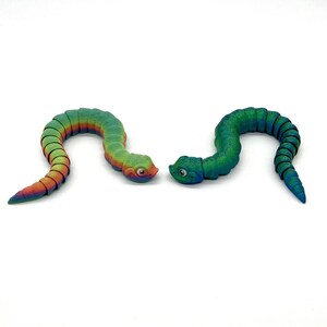 May include: Two colorful segmented toy snakes. One snake is green and blue with a speckled finish. The other snake is rainbow colored with a smooth finish.
