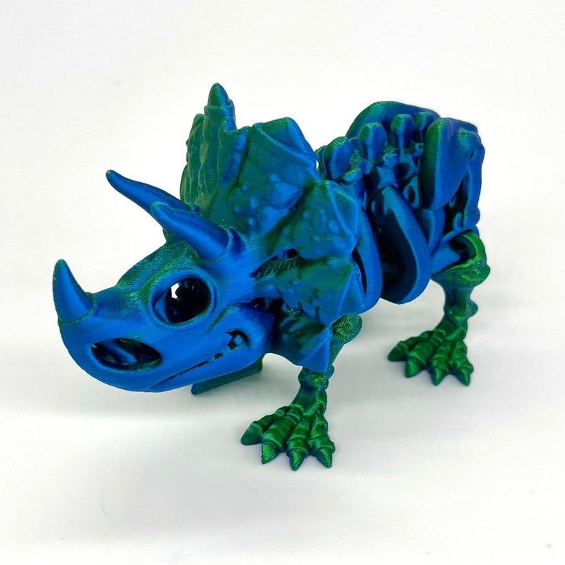 May include: A 3D printed blue and green dinosaur skeleton figurine. The dinosaur is a Triceratops with a large frill and three horns. The figurine is detailed and has a realistic appearance.