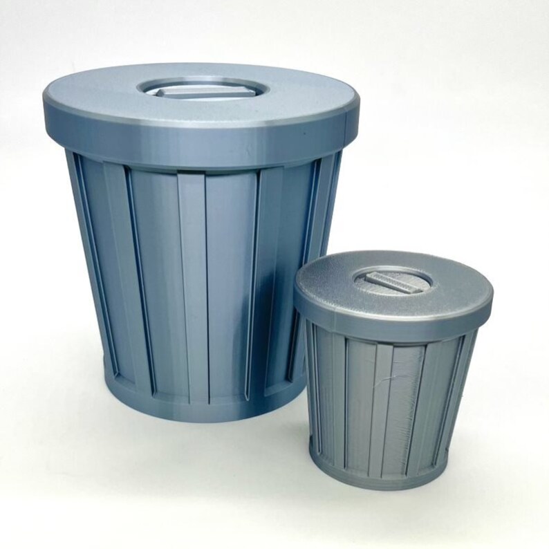 May include: Two blue plastic trash cans with lids. The larger trash can is about 10 inches tall and the smaller trash can is about 5 inches tall.