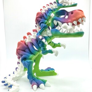 May include: A multi-colored 3D printed dinosaur skeleton with a rainbow color scheme. The dinosaur has three heads and is standing on a white surface.