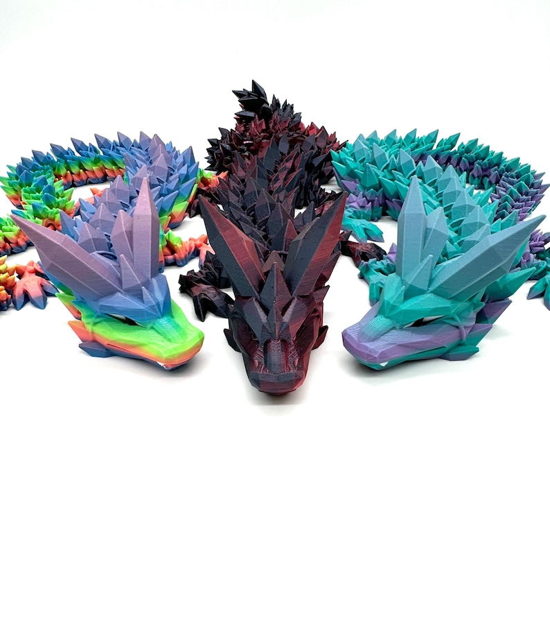 May include: Three 3D printed dragon figurines, each with a different color scheme. The first dragon is a vibrant purple and green, the second is a dark red and black, and the third is a teal and purple.