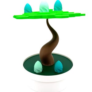 May include: A decorative tree sculpture with a brown trunk, green leaves, and teal-colored egg-shaped accents. The tree sits in a white pot with a dark green base. The sculpture is a modern, abstract design.